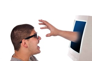 nerdy young man looks frightened as a hand and arm reaches out from his computer monitor a great concept for identity theft or spyware