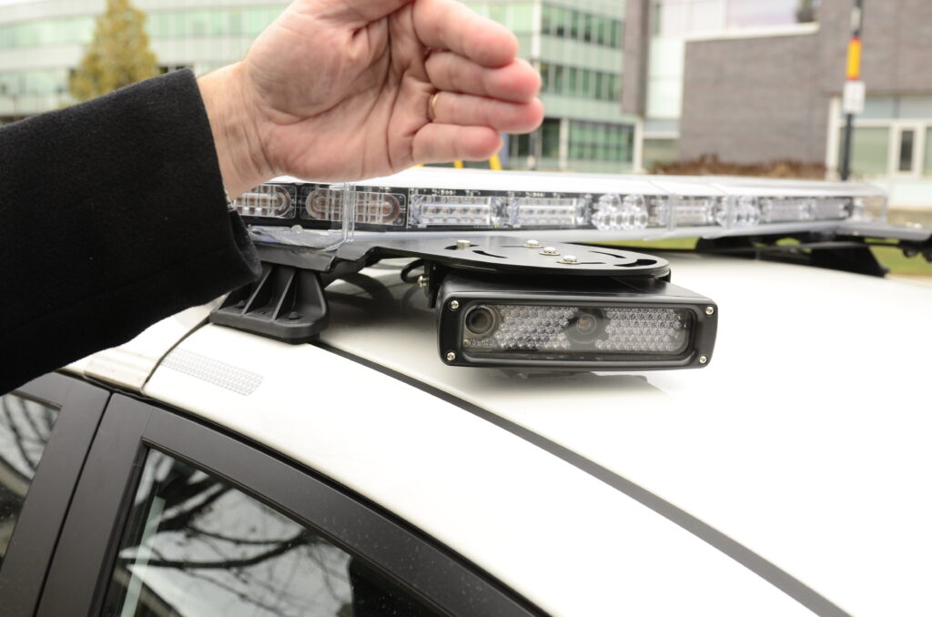 a hand covers an LPR camera mounted to the hood of a security vehicle.